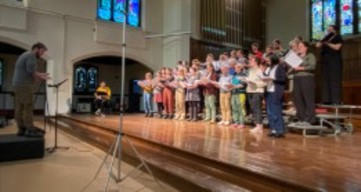 a choir standing on a low stage with the conductor in front of them